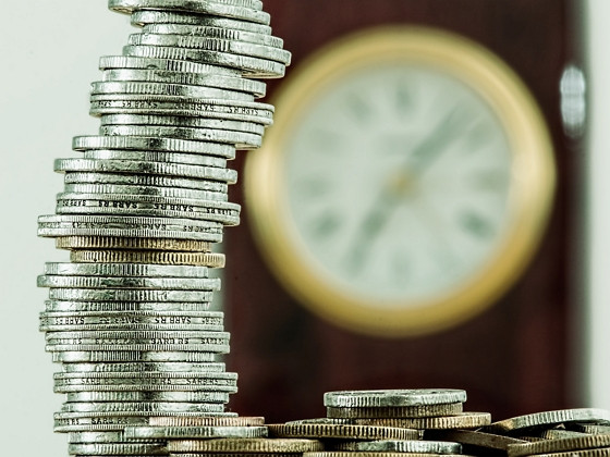 a stack of coins in front of an out of focus clock