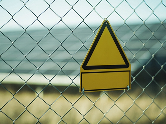 a chain link fence with a yellow triangle sign hanging on it