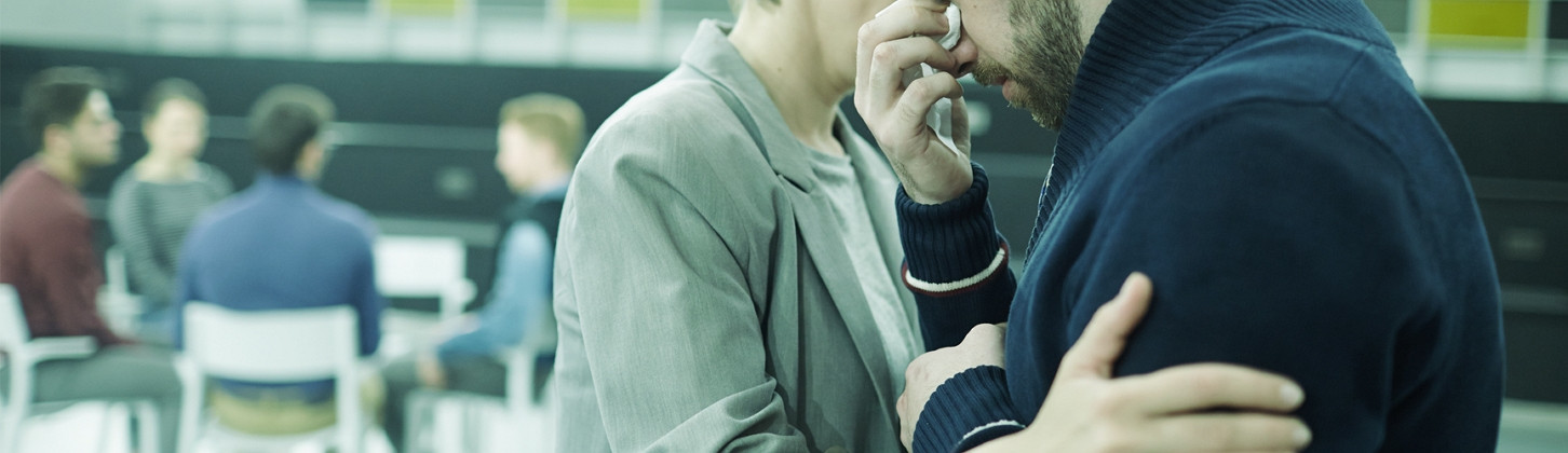 a man crying with another man consoling him while there are four other people in the background