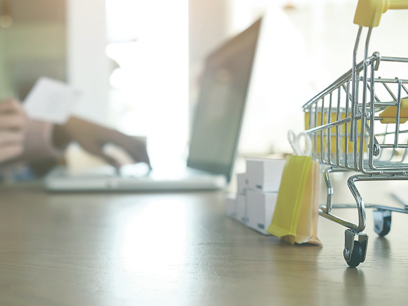 a desk with a laptop and small shopping cart and shopping bags on top of it.